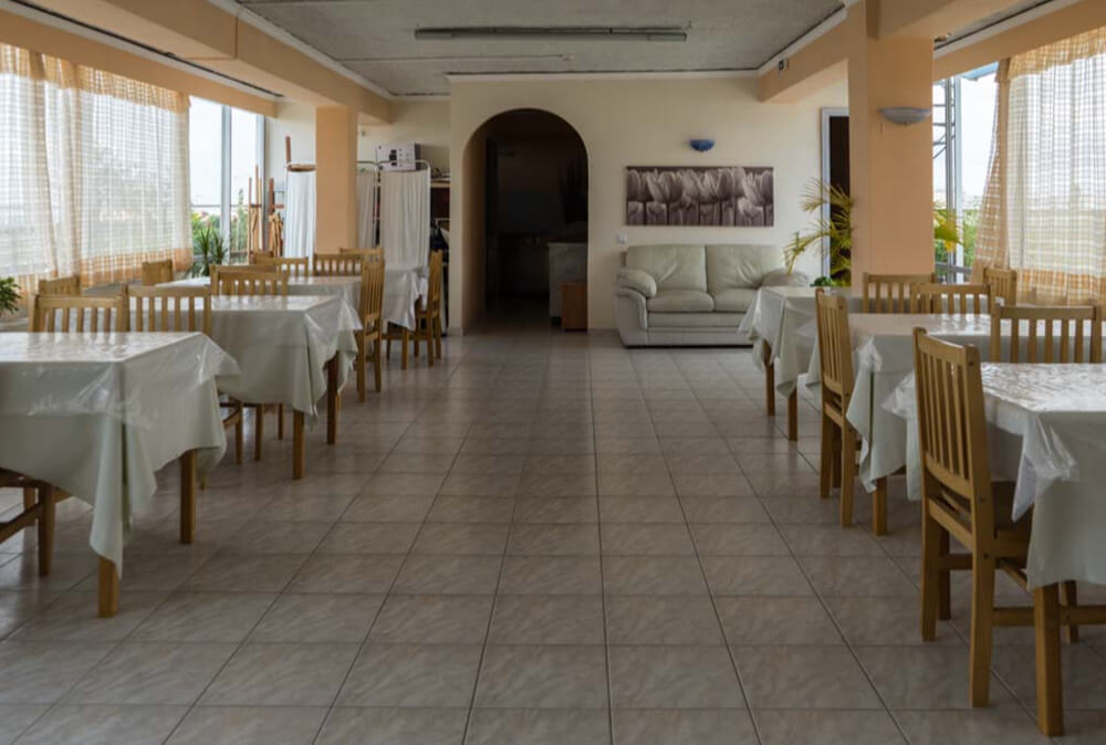 Αίθουσα εστίασης με στρωμένα τραπέζια, ξύλινες καρέκλες και καναπέ στο βάθος